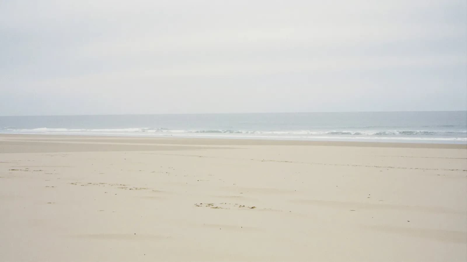Wide empty beach with pale sand and low surf under bright overcast sky
