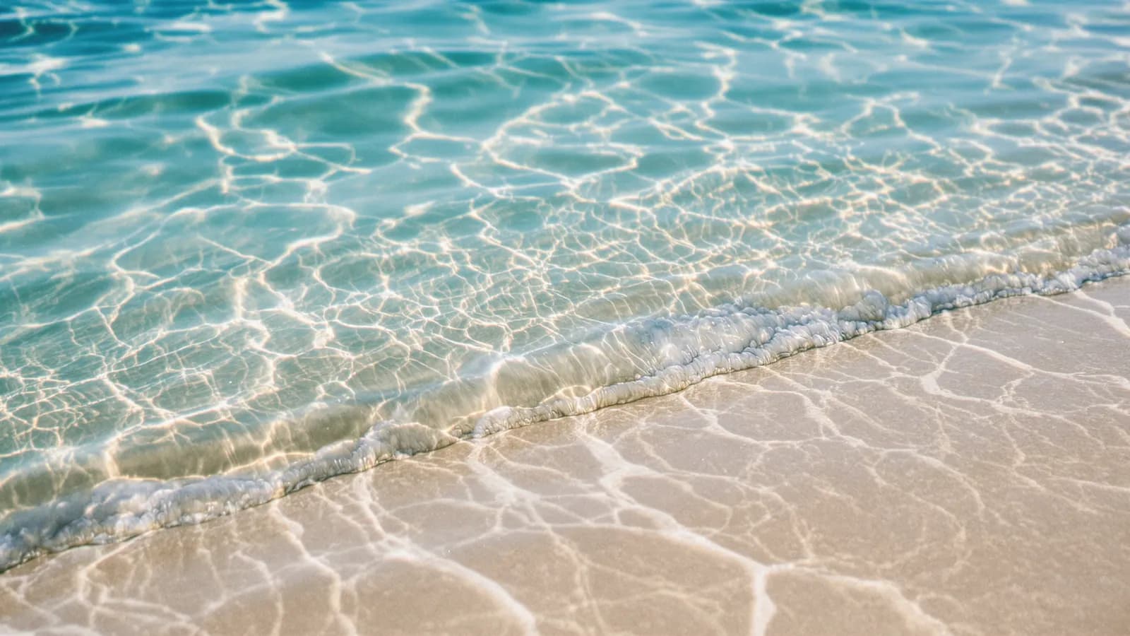 Extreme macro close-up of turquoise sea water rippling over pale sand, sunlight glinting on the surface, shallow depth of field