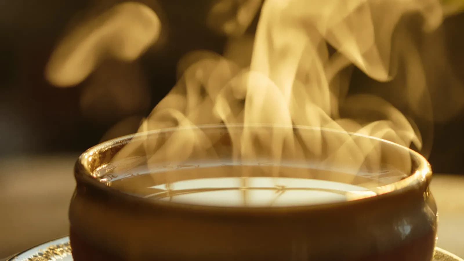 Extreme macro close-up of steam curling off a small copper-toned bowl of milky tea, warm golden light, softly blurred background