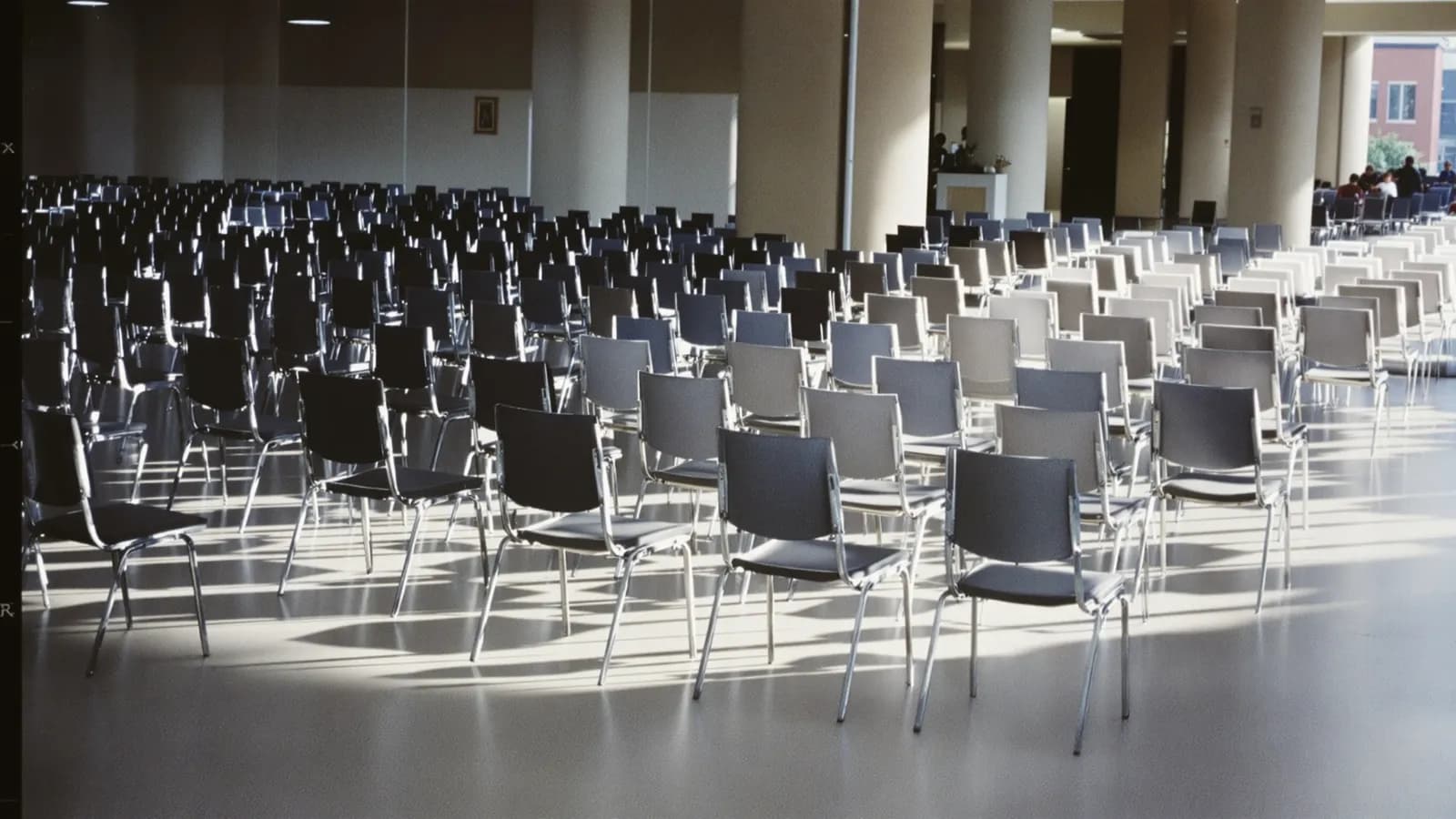 Rows of empty chairs in a bright hall with sunlight across the floor