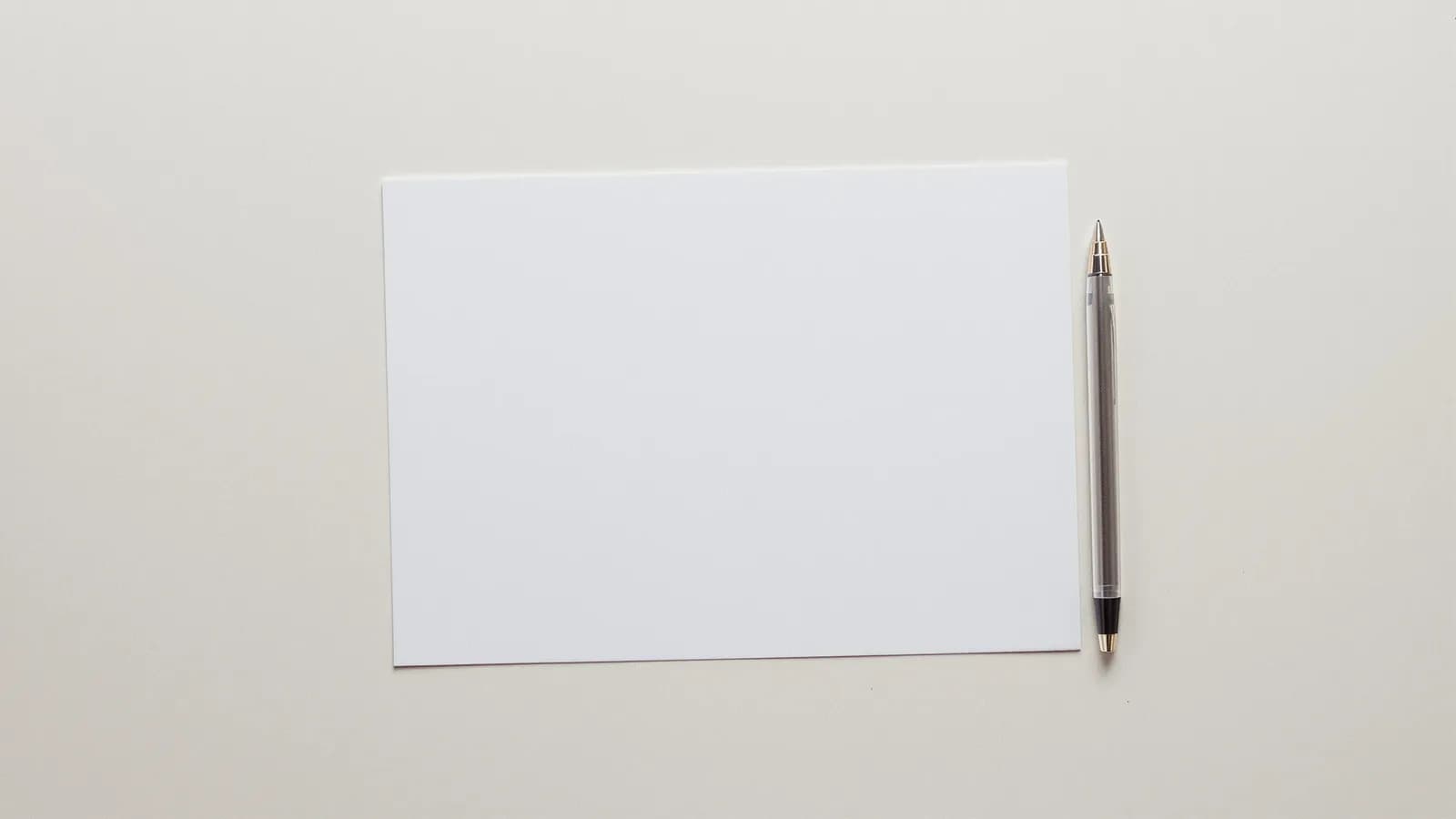 Blank writing paper and a pen on a plain desk in even daylight