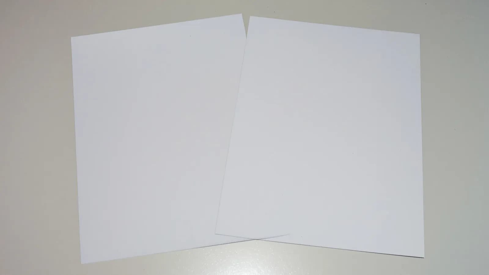 Two sheets of blank paper overlapping on a desk in flat daylight