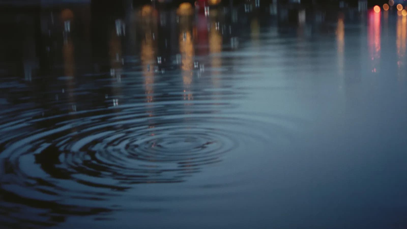 Rain falling on still canal water at dusk with soft blurred reflections