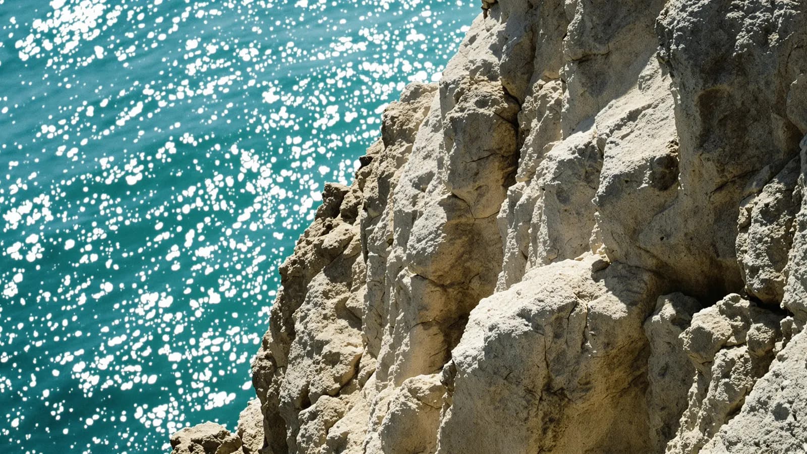 Sunlit limestone cliff texture above a shimmering turquoise sea