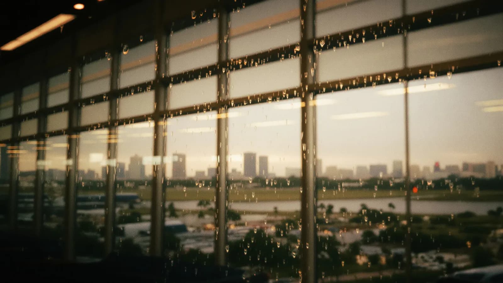 Rain droplets on a glass terminal window with a blurred tropical skyline at dusk