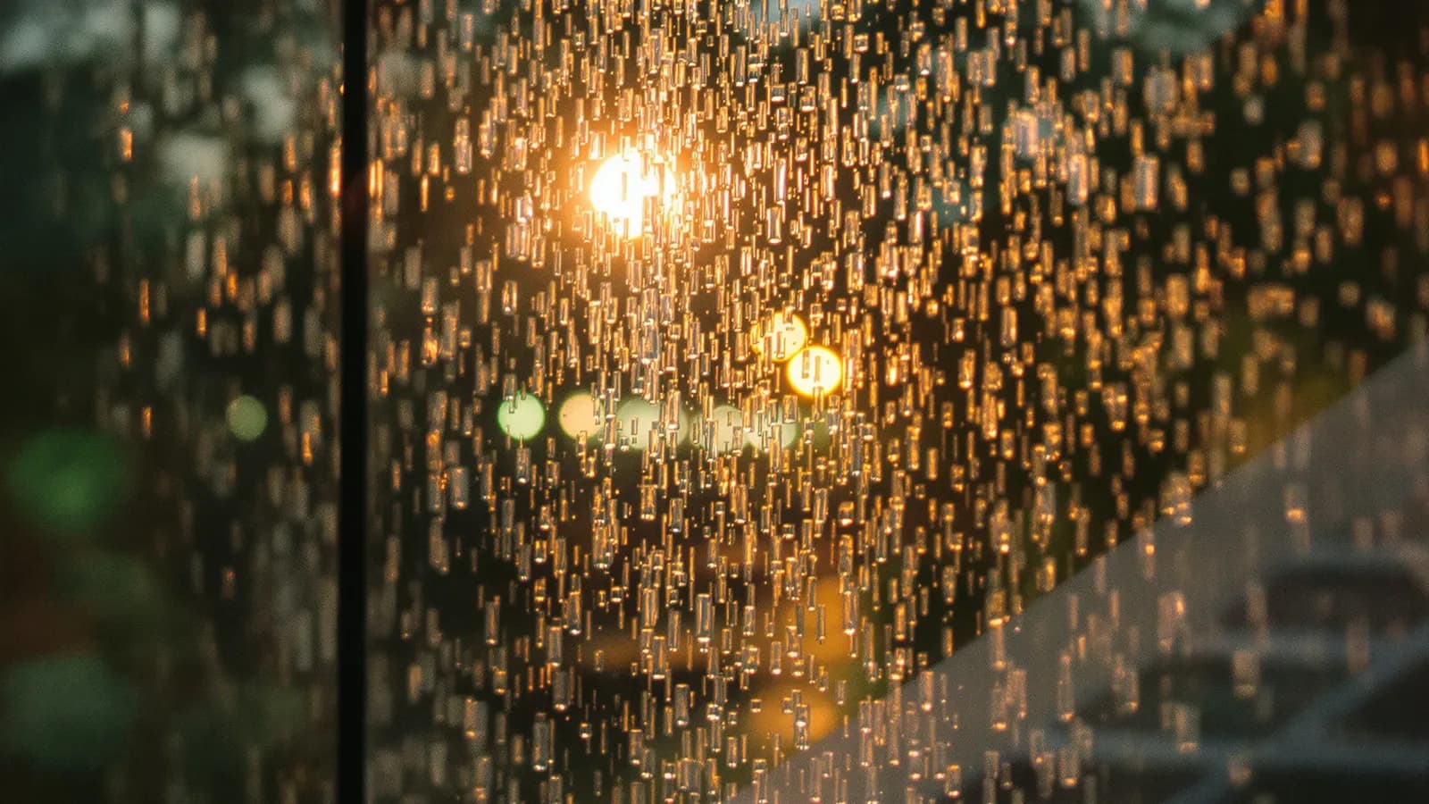 Tropical rain running down a glass wall at dusk with soft light beyond