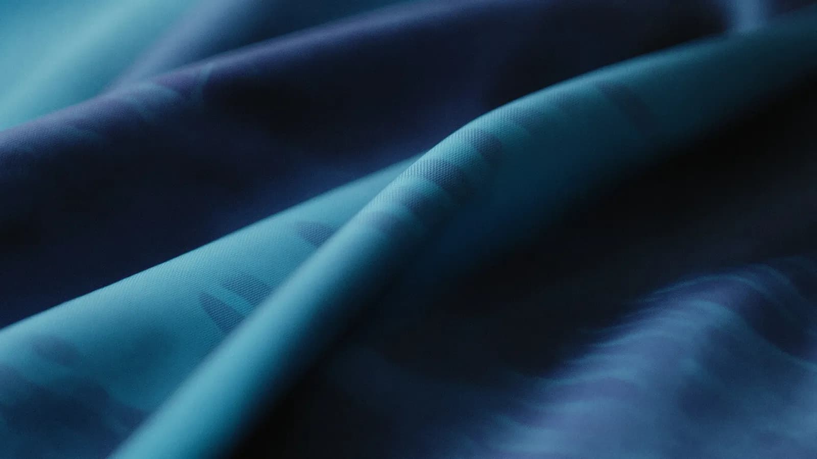 Extreme macro close-up of folded indigo and jade silk fabric with soft directional light
