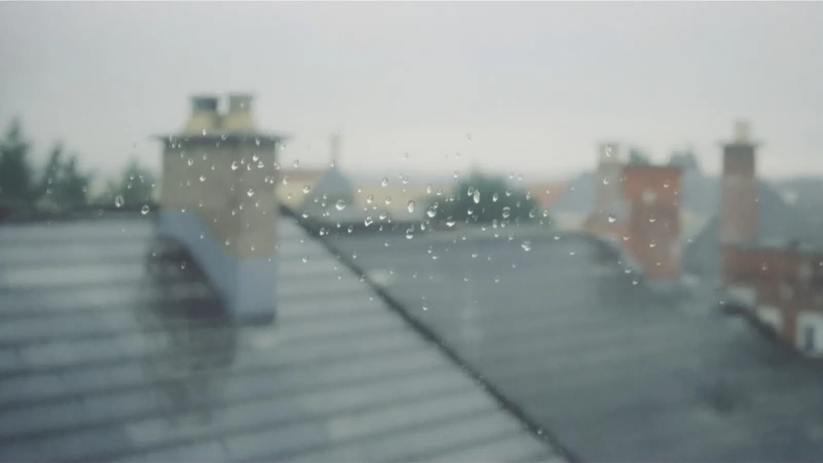 Rain-streaked window with blurred grey city rooftops beyond