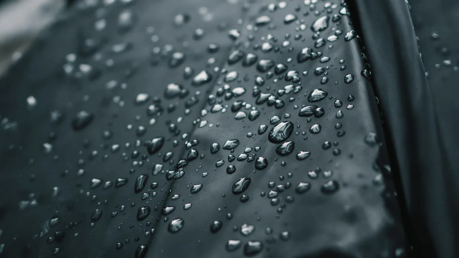 Close-up of raindrops beaded on dark waterproof umbrella fabric