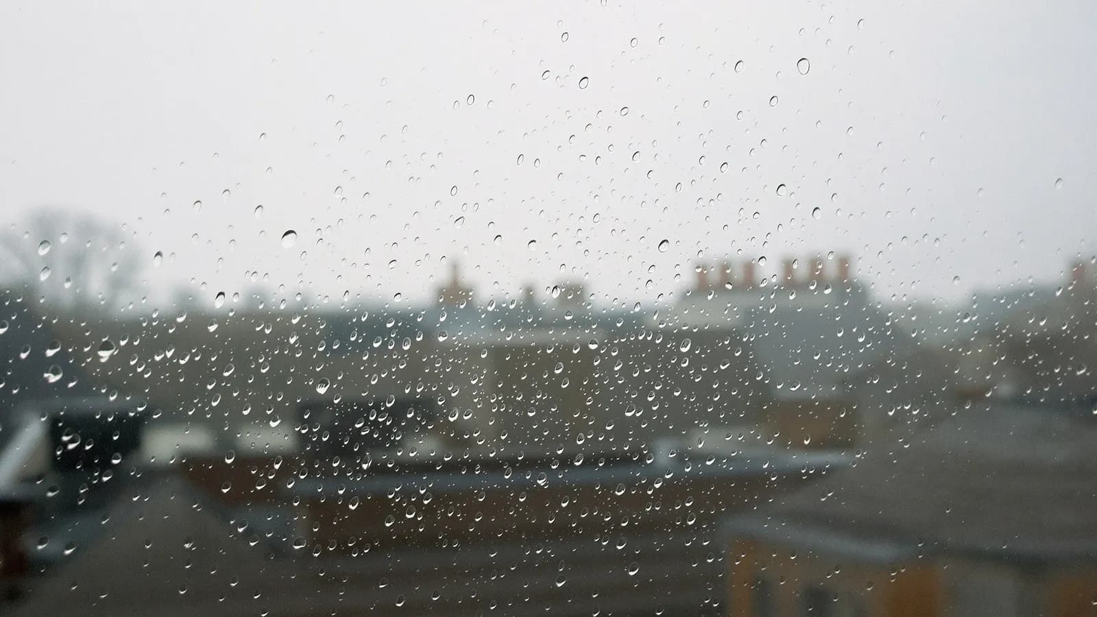 Rain on a window with blurred grey rooftops beyond