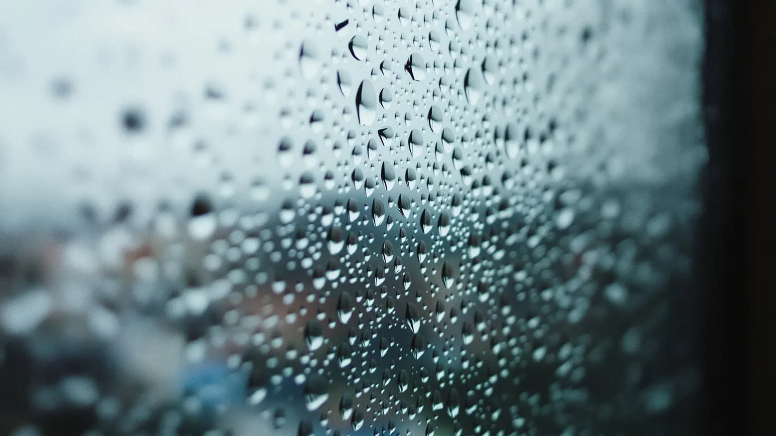 Close-up of rain droplets on a dark window pane with soft grey bokeh