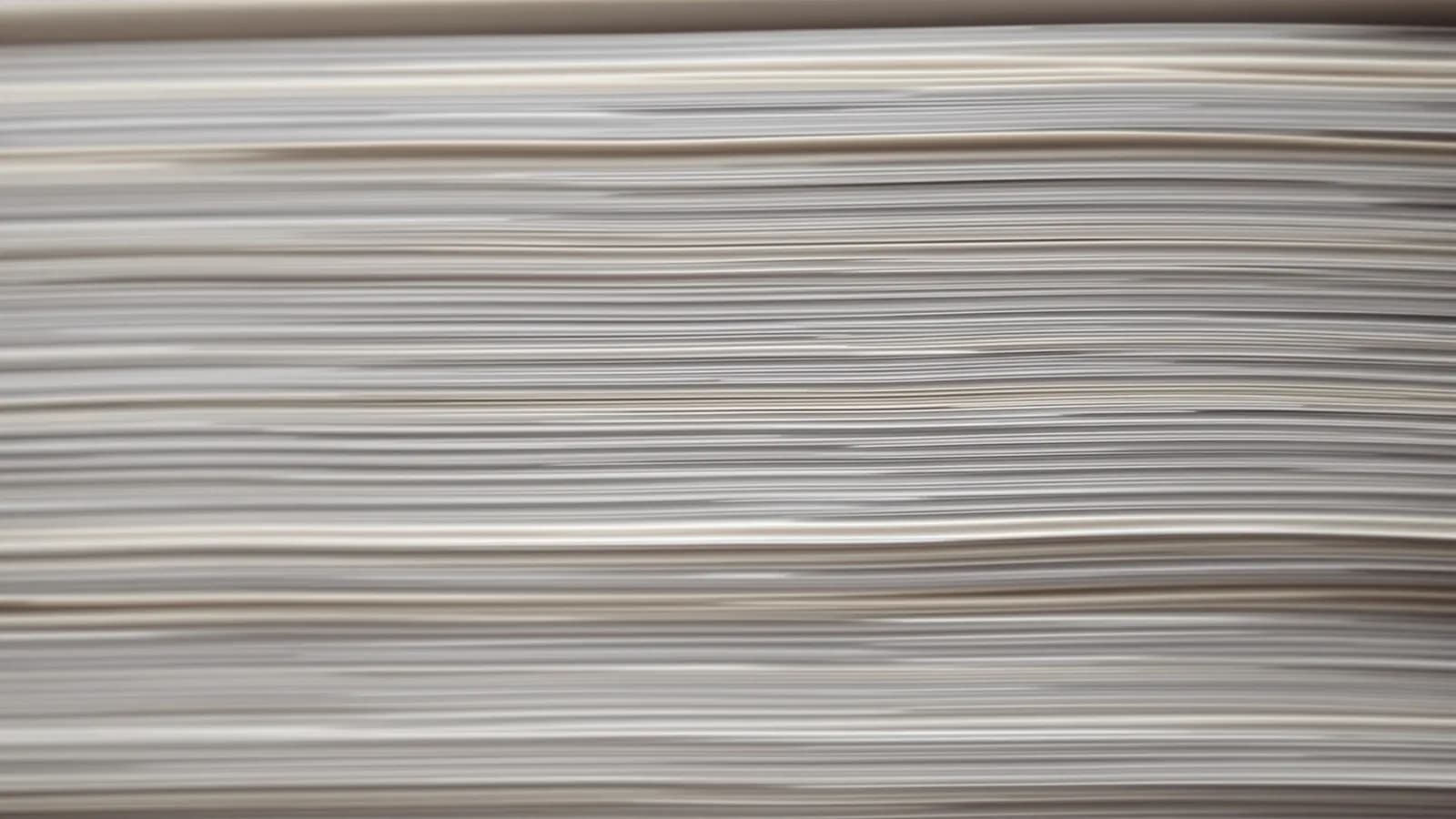 Extreme macro photograph of the cut edges of a tall stack of plain blank paper sheets, warm raking light picking out each layer, very shallow depth of field