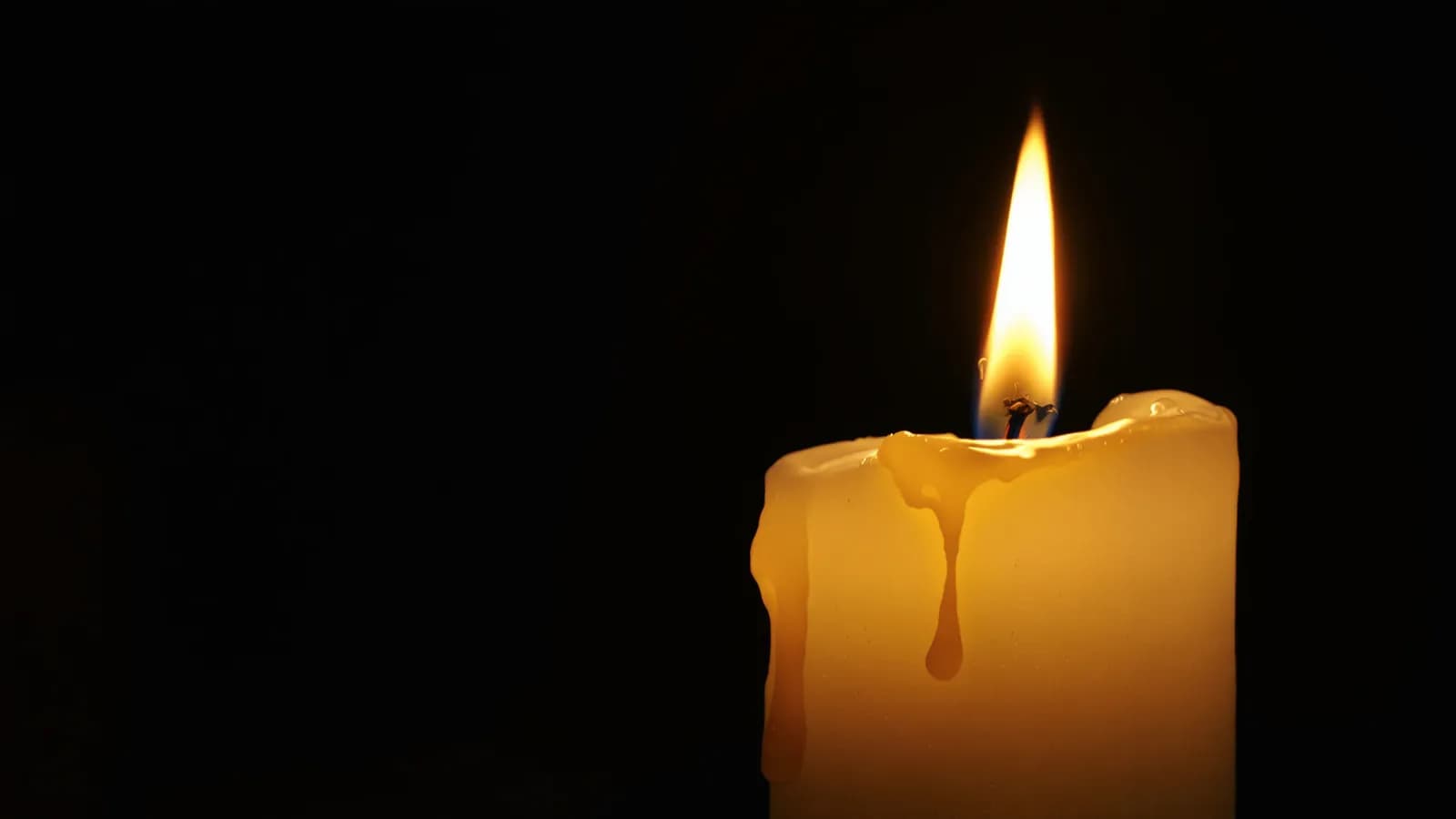 Extreme macro photograph of a lit candle with warm wax dripping down its side against a dark background