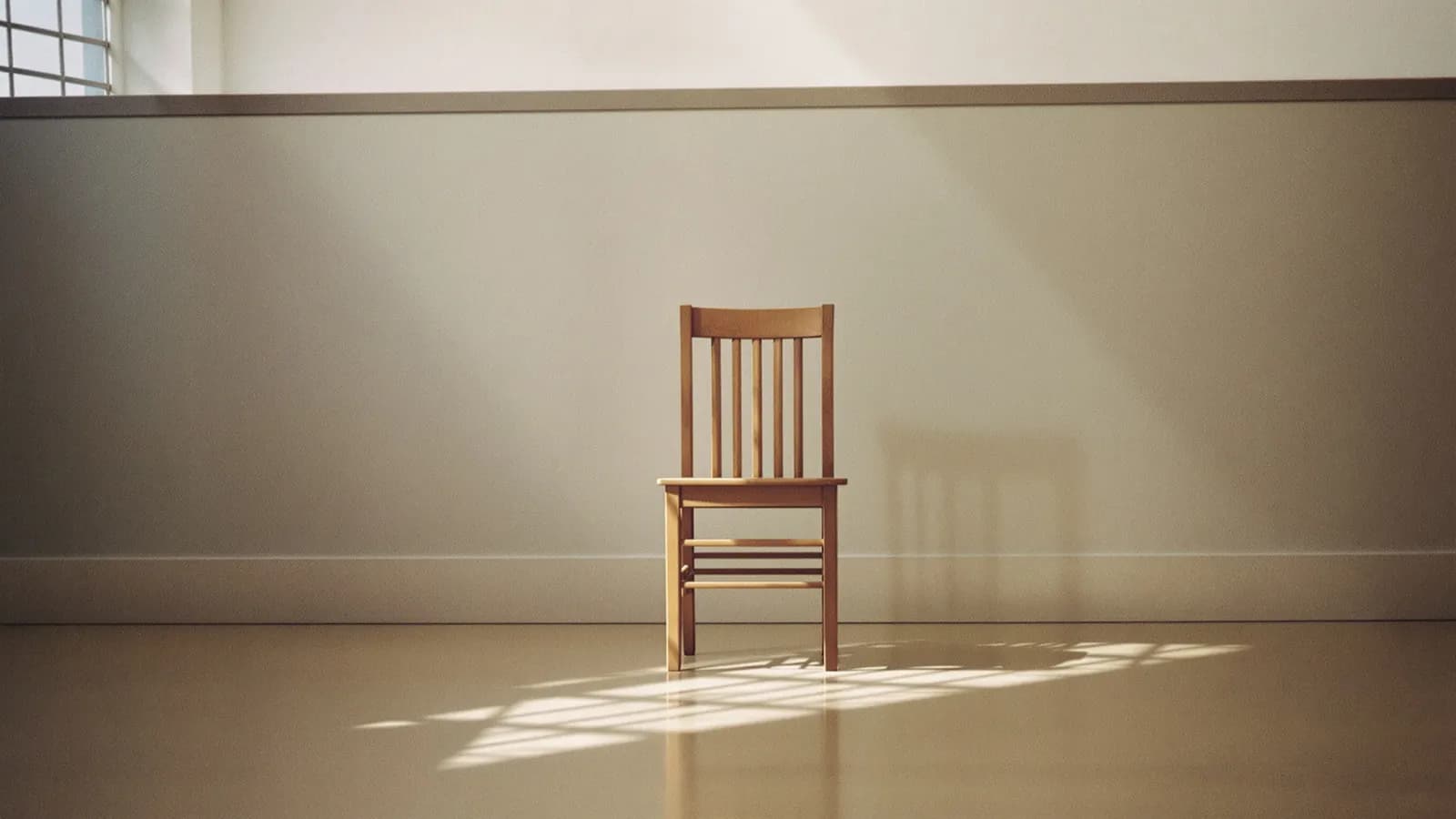 A single empty wooden chair in a quiet room, soft window light across the floor