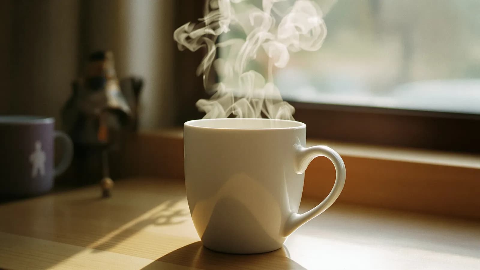 Close-up of steam curling from a plain white ceramic mug in warm morning light
